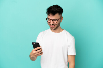 Young caucasian man isolated on blue background sending a message or email with the mobile