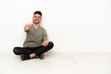Young caucasian man sitting on the floor isolated on white background showing and lifting a finger