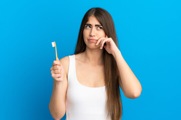Young caucasian woman brushing teeth isolated on blue background having doubts