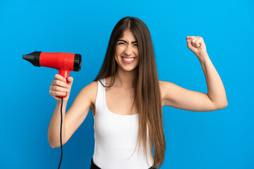 Young caucasian woman holding a hairdryer isolated on blue background doing strong gesture