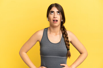 Sport caucasian woman isolated on yellow background looking up and with surprised expression