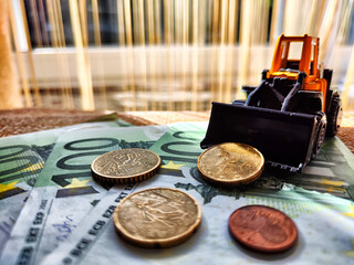 A small toy tractor or excavator on a bundle of money. The concept of the high cost of technology....