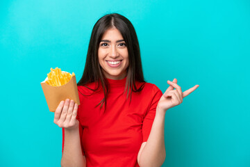 Young caucasian woman catching french fries isolated on blue background pointing to the side to...
