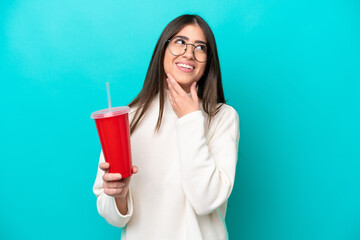 Young caucasian woman drinking soda isolated on blue background looking up while smiling
