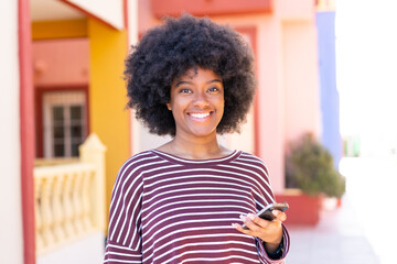 Fototapeta premium African American girl using mobile phone at outdoors smiling a lot