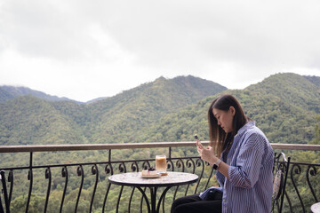 Fototapeta na wymiar digital nomad concept asian freelancer woman use smart phone to work at mountain view of coffeeshop
