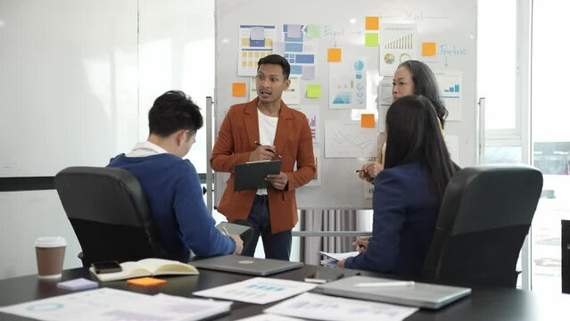 A business team brainstorms during a company meeting and coworkers share ideas about a new marketing plan. Meeting concept and businessmen and women smiling happily at work