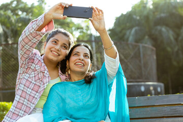 Indian mother and young daughter taking selfie together in outdoor garden, Motherhood , Mother and Daughter relation ship concept