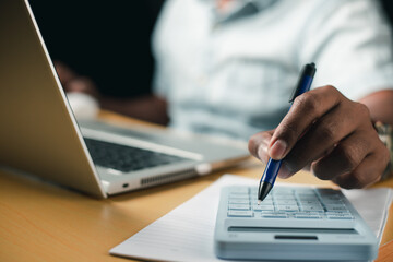 Business accounting concept, businessman using calculator with laptop computer Ready to write a summary of the organization's annual income.
