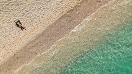 Diagonal aerial view of tropical transparent crystal sea water and woman sunbathing on pebble beach