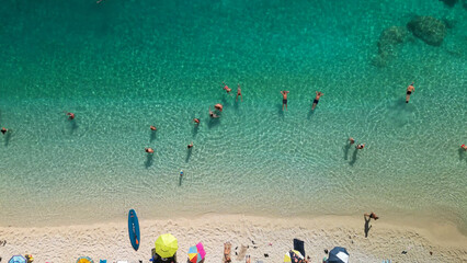 Aerial view of people sunbathing and swimming in turquoise crystal clear sea water