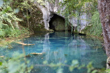 Front view of a cave and beautiful turquoise water on Krupajsko vrelo in Serbia. Background, wallpaper, greeting card, postcard, beautiful nature.