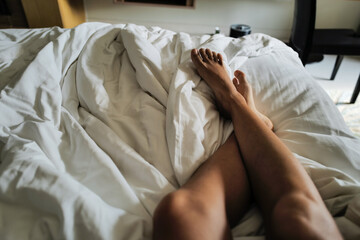 Female legs relaxing on the bed at the hotel - obrazy, fototapety, plakaty