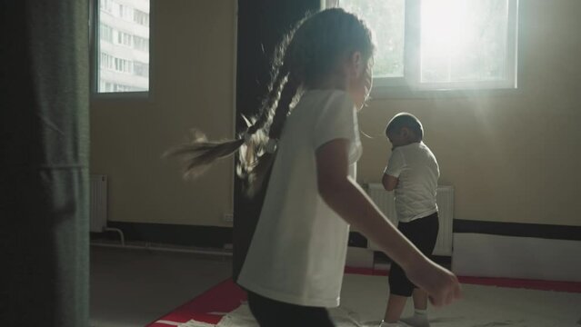 Children exercise with punching bags in sports club. Little martial arts students girl and boy train kickboxing techniques in fighting gym slow motion. Junior fighters