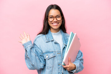 Young student Colombian woman isolated on pink background saluting with hand with happy expression