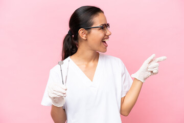 Dentist Colombian woman isolated on pink background pointing finger to the side and presenting a product