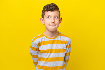 Little caucasian boy isolated on yellow background having doubts while looking up