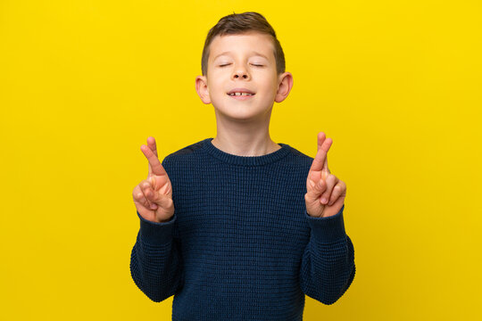 Little caucasian boy isolated on yellow background with fingers crossing and wishing the best