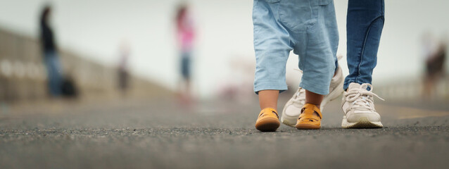 close up leg of infant baby walking on path with mother helping