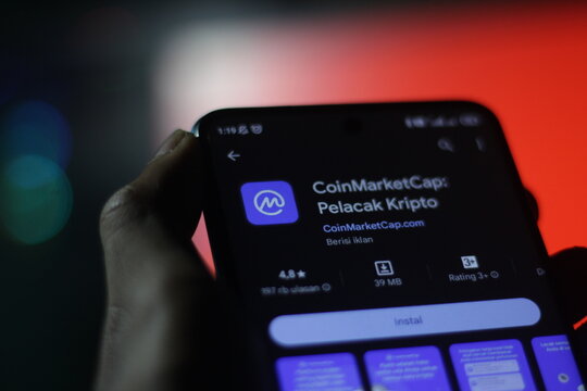 pringsewu, Lampung; November 28, 2023; man's hand holding a mobile phone with the logo of CoinMarketCap or crypto tracker. app store install. selective focus screen.