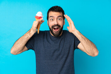 Young man with a cornet ice cream over isolated blue background with surprise expression