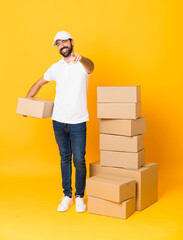 Full-length shot of delivery man among boxes over isolated yellow background points finger at you with a confident expression