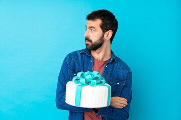 Young handsome man with a big cake over isolated blue background portrait
