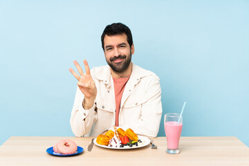 Man at a table having breakfast waffles and a milkshake happy and counting three with fingers