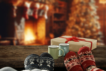 Legs with christmas socks on retro old wooden table. Empty space for your decoration. Home interior with fireplace and magic time in december. Mockup place for your decoration.Warm dark light.