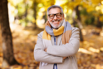 Portrait of happy positive mature man with broad smile    in elegant clothes on an autumn walk   in city park - obrazy, fototapety, plakaty