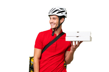Pizza delivery man with work uniform picking up pizza boxes over isolated background looking to the side and smiling