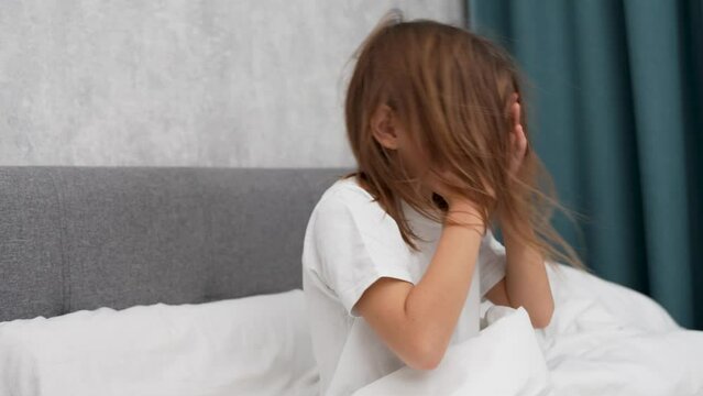 Child girl is sneezes snot into napkin on bed at home