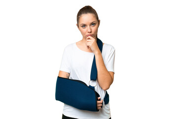 Young blonde woman with broken arm and wearing a sling over isolated chroma key background thinking
