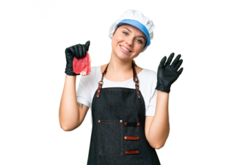 Butcher woman wearing an apron and serving fresh cut meat over isolated chroma key background saluting with hand with happy expression