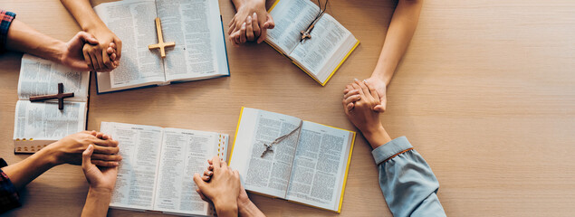 Cropped image of group of people praying together while holding hand on holy bible book at wooden...