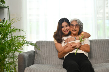 Affectionate young Asian woman hugging senior mother from back. International hug day concept