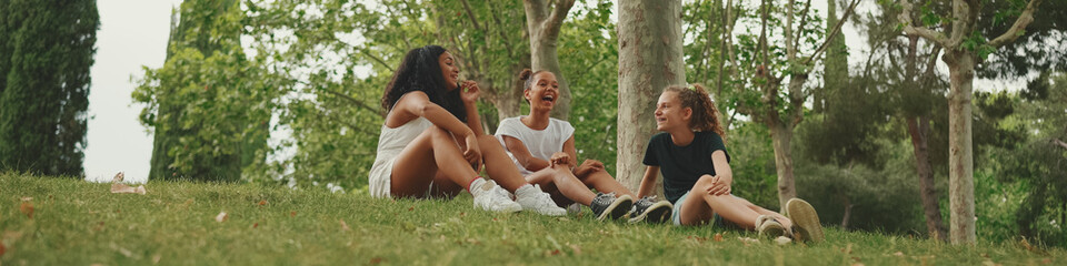 Three girls friends pre-teenage sit on the grass in the park and emotionally talking. Three teenagers on the outdoors