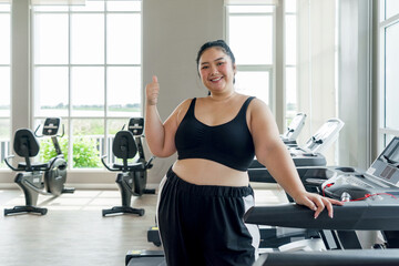 A plus-sized woman is standing on a treadmill in a gym, preparing to start her exercise routine...