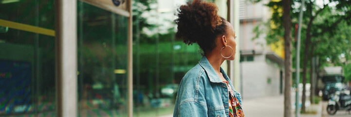 Cute African girl with ponytail, wearing denim jacket, in crop top with national pattern, standing...