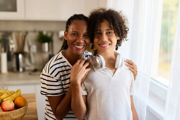 Portrait of embraced teenage boy and his mother at home