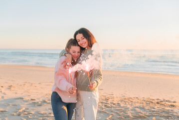 Delighted lesbian couple holding sparklers on beach
