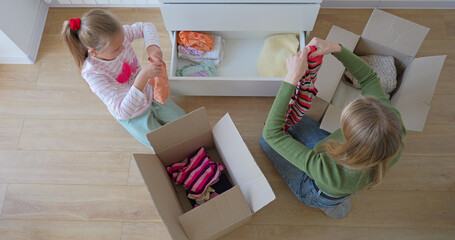 Little girl with mother putting clothes to drawer in bedroom after moving