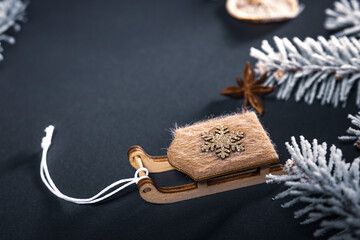 A sleigh with a star on a dark table among dried pieces of orange and cinnamon and branches of a Christmas tree covered with snow