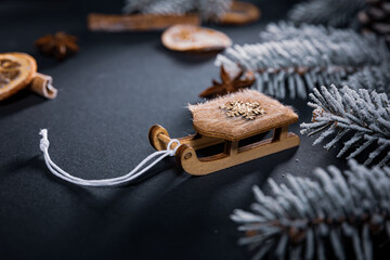 Fototapeta premium A sleigh with a star on a dark table among dried pieces of orange and cinnamon and branches of a Christmas tree covered with snow