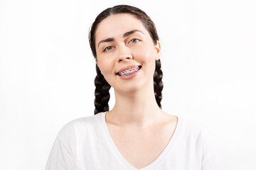 Portrait of smiling Caucasian young woman with ligature braces on her teeth. White background. Concept of orthodontic treatment and dentistry