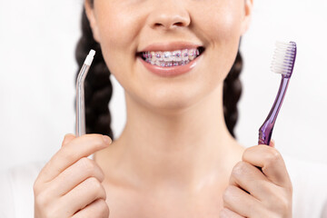 Close up of young smiling woman with brackets on teeth show manual toothbrush and monopuckle brush....