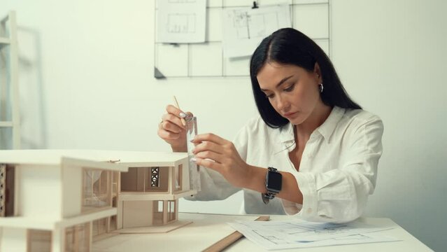 Closeup of beautiful young architect engineer focus on using pencil marking point and ruler to measure house model at modern office with blueprint. Creative design and architect concept. Immaculate.