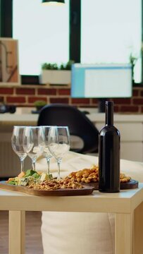Vertical video Panning shot of empty cozy apartment living room with appetizer platter and wine bottle on wooden table, awaiting guests to arrive. House interior with leather couch and TV running in
