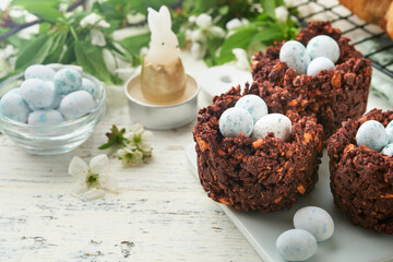 Easter brunch or breakfast. Easter chocolate nest cake with chocolate candy eggs, traditional hot cross buns and deviled eggs with bouquets of blooming apple trees. Spring Easter holiday food concept.