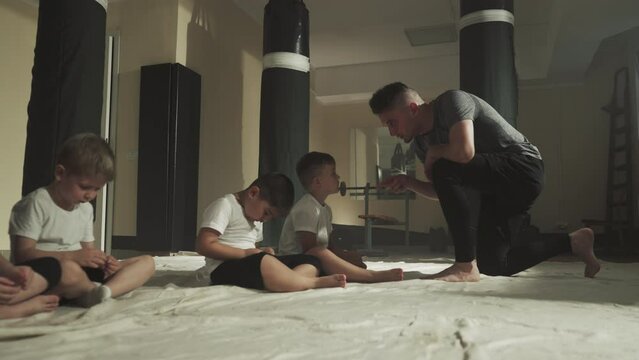 Trainer scolds bad student in martial arts club. Little children listen to professional instructor sitting on floor in gym slow motion. Combat lesson